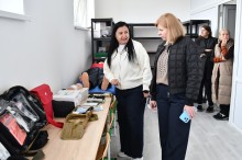 Начальник Мангушської селищної військової адміністрації Наталія Воробйова роздивляється вироби у школі мистецтв, поруч жінка щось розповідає.