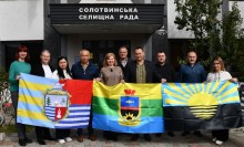 Спільне фото. Члени делегації біля фасаду Солотвинської селищної ради тримають прапори громад та Донеччини.