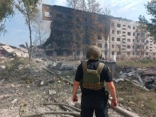 Правоохоронець стоїть біля зруйнованого окупантами багатоквартирного будинку