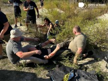 Один чоловік лежить на землі, поруч двоє відпрацьовують навички надання медичної допомоги. З іншої сторони іде жінка в імітованому бойовому окопі