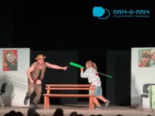 Театральна сцена: актор тікає, акторка з зеленою палицею рухається за ним; на тлі — фото на білих панелях.