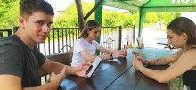 Хлопець та дві дівчини сидять на вулиці за столом, тримають в руках мобільні телефони, за допомогою яких долучились до інтерактивної вікторини «Україна — моя держава».