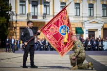 Володимир Зеленський тримає прапор ЗСУ а поруч на одному коліні стоїть військовий