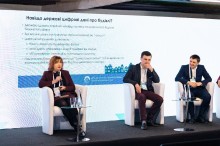 Представники міністерства та посадовці, сидять на білих кріслах, жінка щось розповідає.