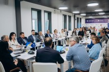 Загальний вигляд конференц-залу Маріупольського університету під час засідання, де велика група людей бере участь у дискусії за довгим столом.