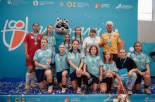 Дівоча команда з футзалу стоїть з тренером і тримає нагороди.