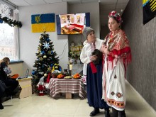 Сценічна дія. Дівчина в українському вбранні та хлопець. Позаду них ялинка та стіл вкритий рушником.