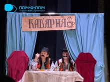 Актори на сцені у народних костюмах сидять за столом, зверху на декорації надпис "кав'ярня".