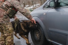 Арчі уважно оглядає переднє колесо автомобіля, поруч військовий.
