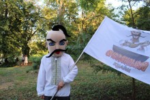 Чоловік, одягнений у національному вбранні. На обличчі маска козака. Тримає прапор заходу.