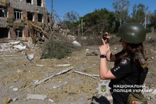 Жінка полійейська фотографує зруйновану будівлю