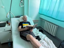 Захисник лежить на лікарняному ліжку, в руках тримає книгу, яку йому подарували представники Гродівської громади.