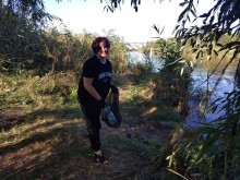 Дівчина біля водоймища збирає сміття у мішок