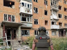 Правоохоронець стоїть на фоні зруйнованого багатоквартирного будинку