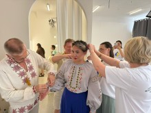 Кілька людей допомагають моделі вдягнути традиційну українську вишиту сорочку в інтер'єрі студії