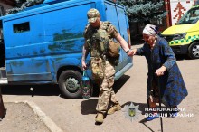 Поліцейський веде бабусю з палицею до евакомобіля