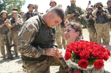 Військовий надіває каблучку нареченій з квітами в руках, поруч стоять бійці