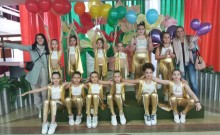 Дівчата з творчого танцювального колективу в блискучих золотих костюмах сидять і стоять, тримаючи різнокольорові повітряні кульки.
