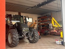 Трактор з великими колесами стоїть у гаражі, поруч шафа з інструментом.