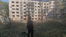 Правоохоронець на фоні зруйнованої багатоповерхової будівлі.