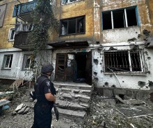 Правоохоронець стоїть біля зруйнованого окупантами багатоповерхового будинку