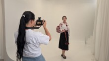 Фотографиня знімає дівчину в українському національному строї з чорною спідницею на білому тлі студії