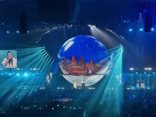 Дія на сцені концертного залу. Величезна куля, в якій відображається місто та ялинка. Співаки на сцені співають.