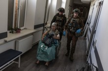 Парамедики везуть літню жінку на кріслі колісному у приміщенні закладу