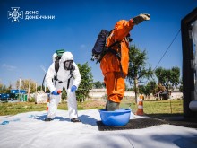 Двоє рятувальників. Один у білому другий у помаранчевому захисному костюмі. На навчаннях з ліквідації хімічної атаки.