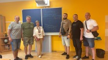 Спільне фото учасників делегації біля дошки, на якій українською мовою написано "Україна переможе".