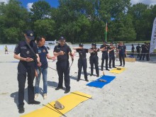 Курсанти у поліцейській формі, шикувавшись у ряд, тренуються стрільбі з лука на пісчаному майданчику під наглядом інструктора.