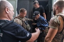Поліцейські та волонтер допомогають літньому чоловіку виходити з автомобіля.