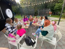 Жінки-педагогині із дітьми зібралися за столиками біля кафе, сидять у колі та спілкуються.