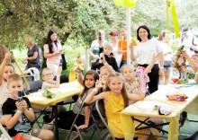 Діти та дорослі на природі сидять за столами та показують поробки