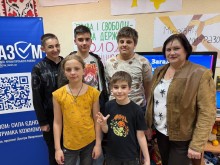 Група дітей і доросла жінка усміхаються, позуючи на фоні банера «МиРазом» і патріотичних плакатів у кімнаті для ігор