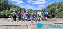 Спільне фото велотуристів на дерев'яному мосту. Вони тримають велосипеди за руль, позаду річка.