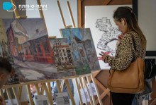 Шанувальниця творчості художниці уважно з захопленням вдивляється у пейзажі міста на картинах.