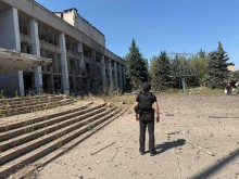 Правоохоронець стоїть біля пошкодженої окупантами адміністративної будівлі