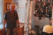Військовий у формі стоїть у кімнаті, прикрашеній військовими шевронами та картою
