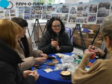 Жінки сидять за круглим столом, спілкуються та роблять сувеніри.