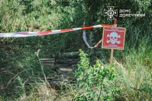 На березі лежать витягнуті з водойми вибухонебезпечні предмети. Місце обтягнуте біло-червоною стрічкою та стоїть табличка про мінну небезпеку.