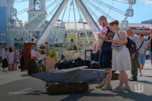 Чоловік з дитиною на руках та молода жінка уважно роздивляються уламок дрону, який привезений з міста Часів Яр.
