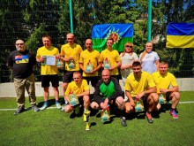 Футбольна команда, спільне фото. Позаду прапори України та громади. Поруч Вікторія Набокова, Артур Насібян, дружина полеглого захисника з Краматорська Вікторія Ільєнко.