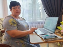 Жінка сидить за столом біля відкритого ноутбука та бере участь у вебінарі.