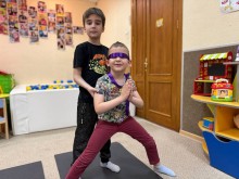Хлопчик допомагає іншому хлопчику з пов'язкою на очах, займатись йогою