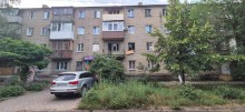 Юагатоповерхівка з пошкодженими вікнами та автомобіль поруч з будівлею.