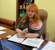 Вікторія Набокова, сидить за столом. На столі ноутбук та папери.
