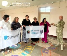Вчителі передають військовому саморобні браслети від дітей. На передньому плані тримають прапори громади.