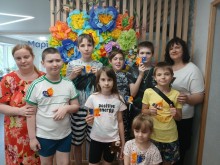 Група дітей і педагогів на фоні квіткової інсталяції демонструють патріотичні поробки до Дня Конституції України.