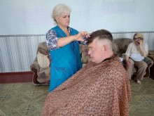 Жінка-перукар стоїть біля чоловіка, якому підстригає волосся.